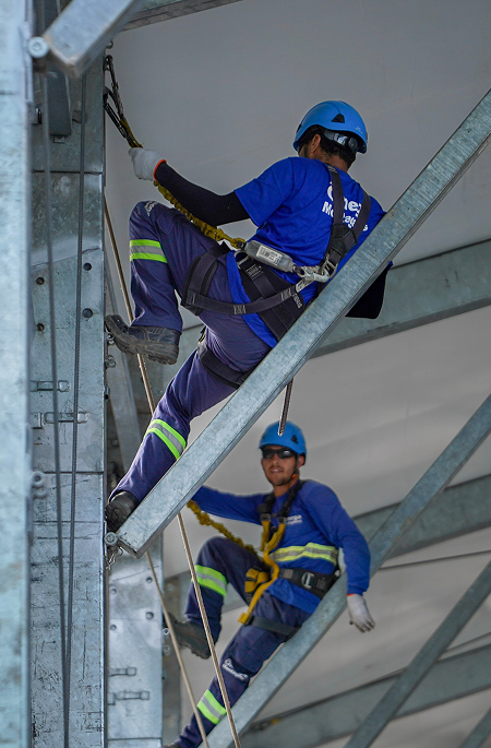 Montadores com capacete e cinto de segurança durante a montagem da estrutura